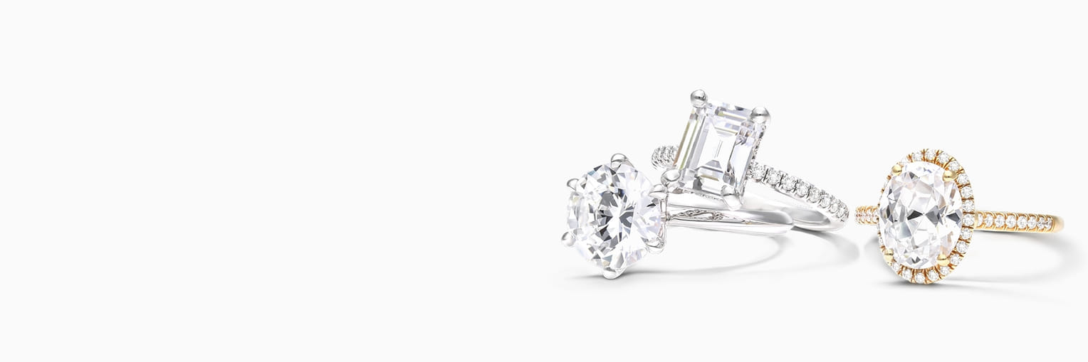 Three elegant diamond rings featuring different cuts: round, emerald, and oval, set in silver and gold bands on a white background.