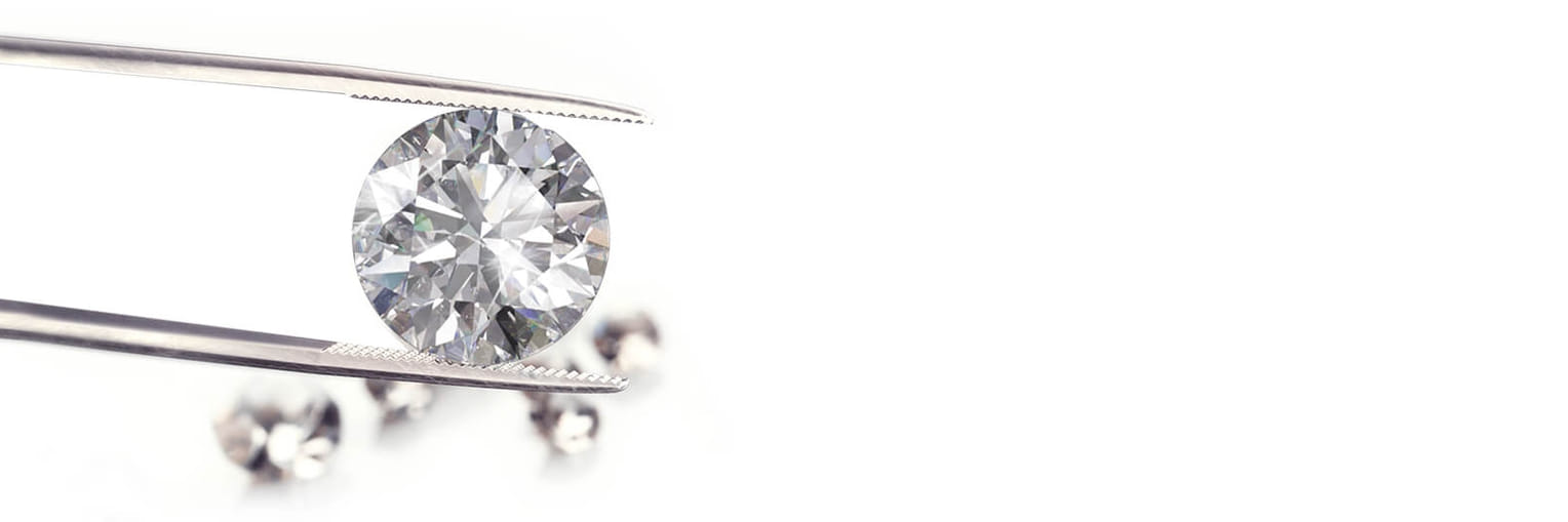 A round, sparkling diamond held by tweezers with a soft focus on additional diamonds in the background."