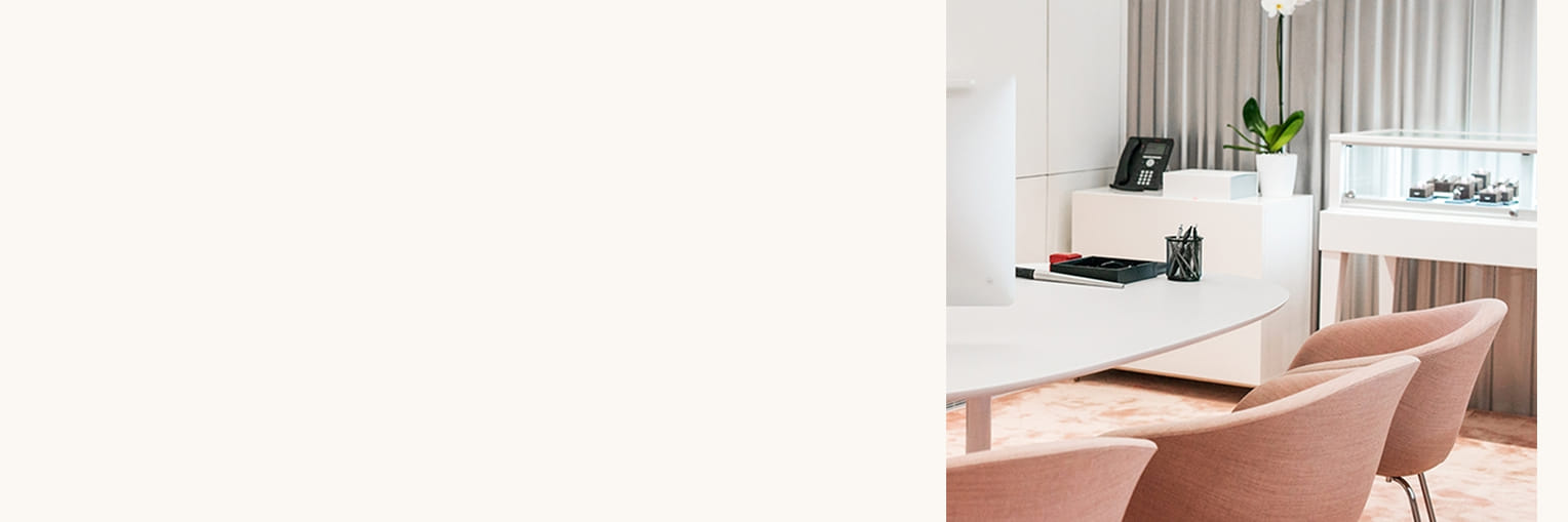 Modern office interior with a curved desk, pink chairs, a computer, phone, potted plant, and display case."