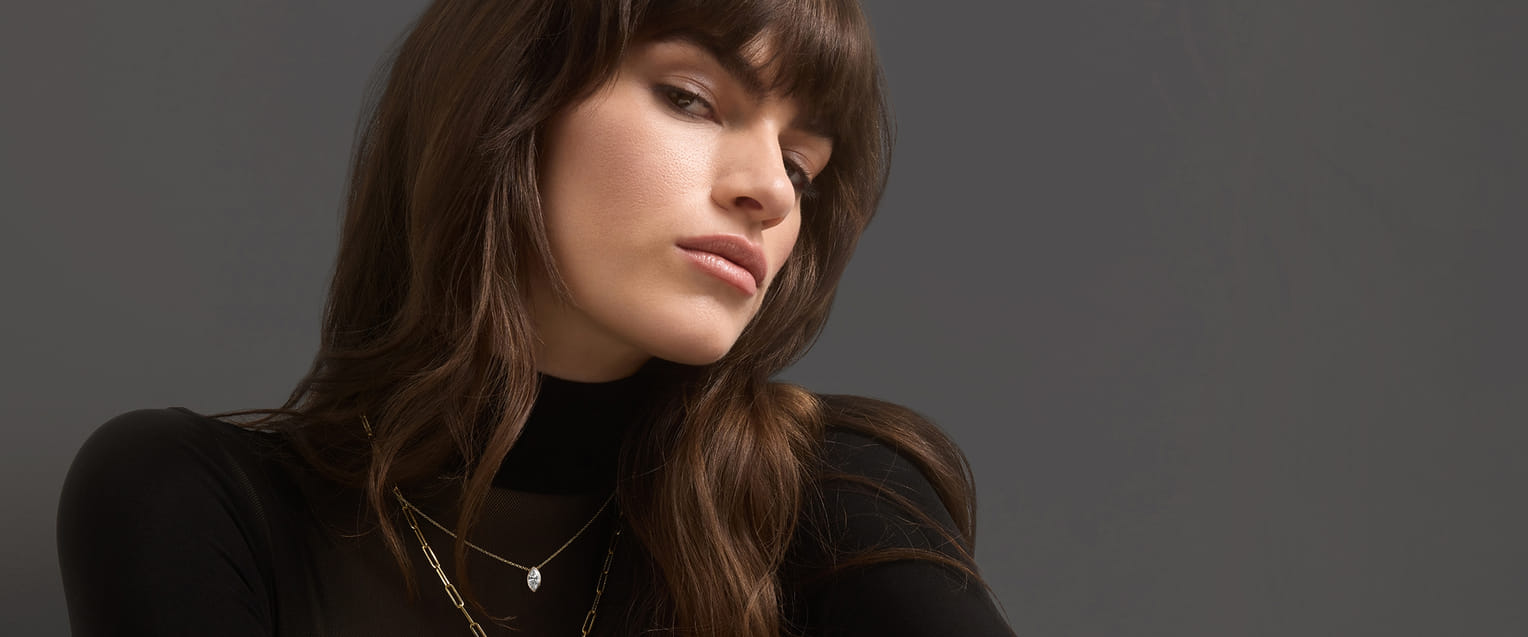 Person holding a necklace with a large diamond pendant, smiling.